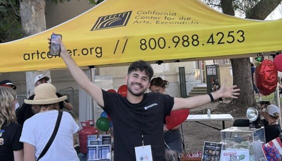 Brandon Hayes with his arms out wide in front of a yellow CCAE pop-up cover at a street fair.