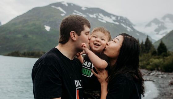 Photo of a couple holding a young child in front of an alpine lake