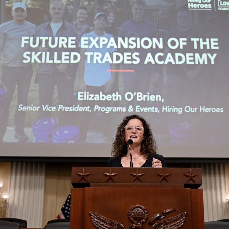 Senior Vice President, Programs & Events at Hiring Our Heroes Elizabeth O'Brien speaks at a podium while presenting the future expansion of the Skilled Trades Academy. 
