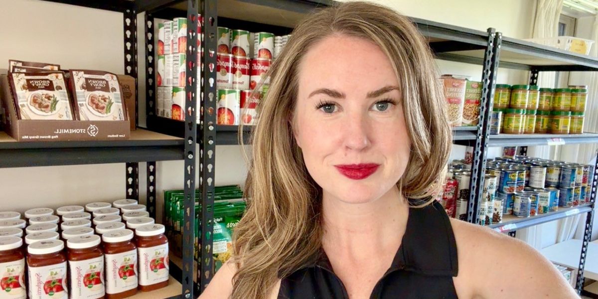 Close up of Megan Rowley standing in front of shelves of food at the JBAB food pantry.