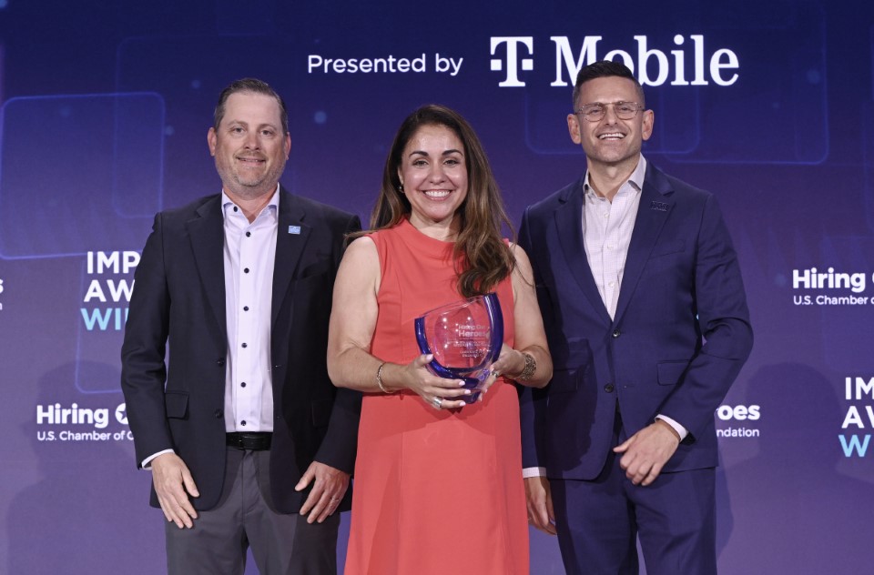 Three people pose with the Military Spouse Entrepreneur Impact Award. Gabi Bell is in the center holding her award. 