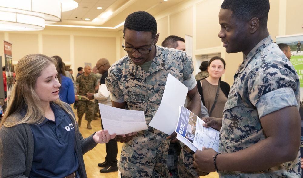 A woman employer provides two service members documents about her company at a hiring fair.