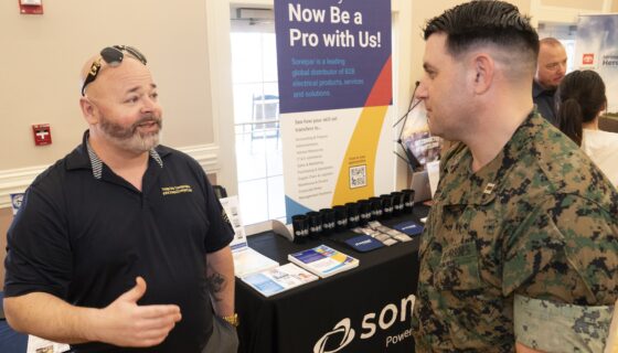 A marine talking to an employer in front of a hiring fair booth.