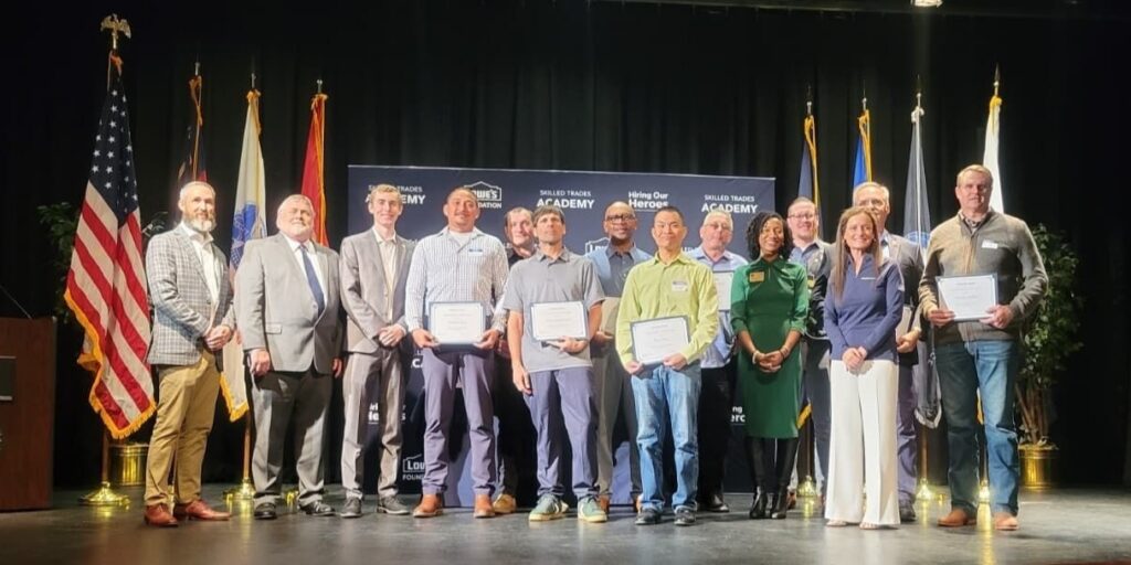 Image of all the Skilled Trades Academy graduates on stage with flags and Hiring Our Heroes backdrop