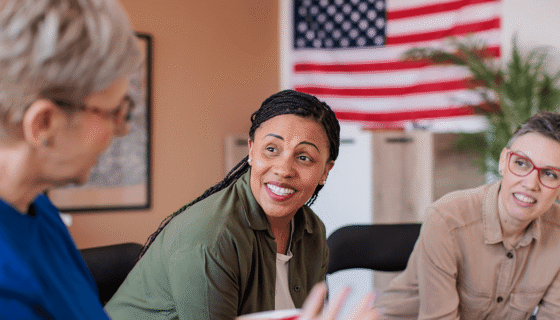 Three veterans chat with an American flag behind them.